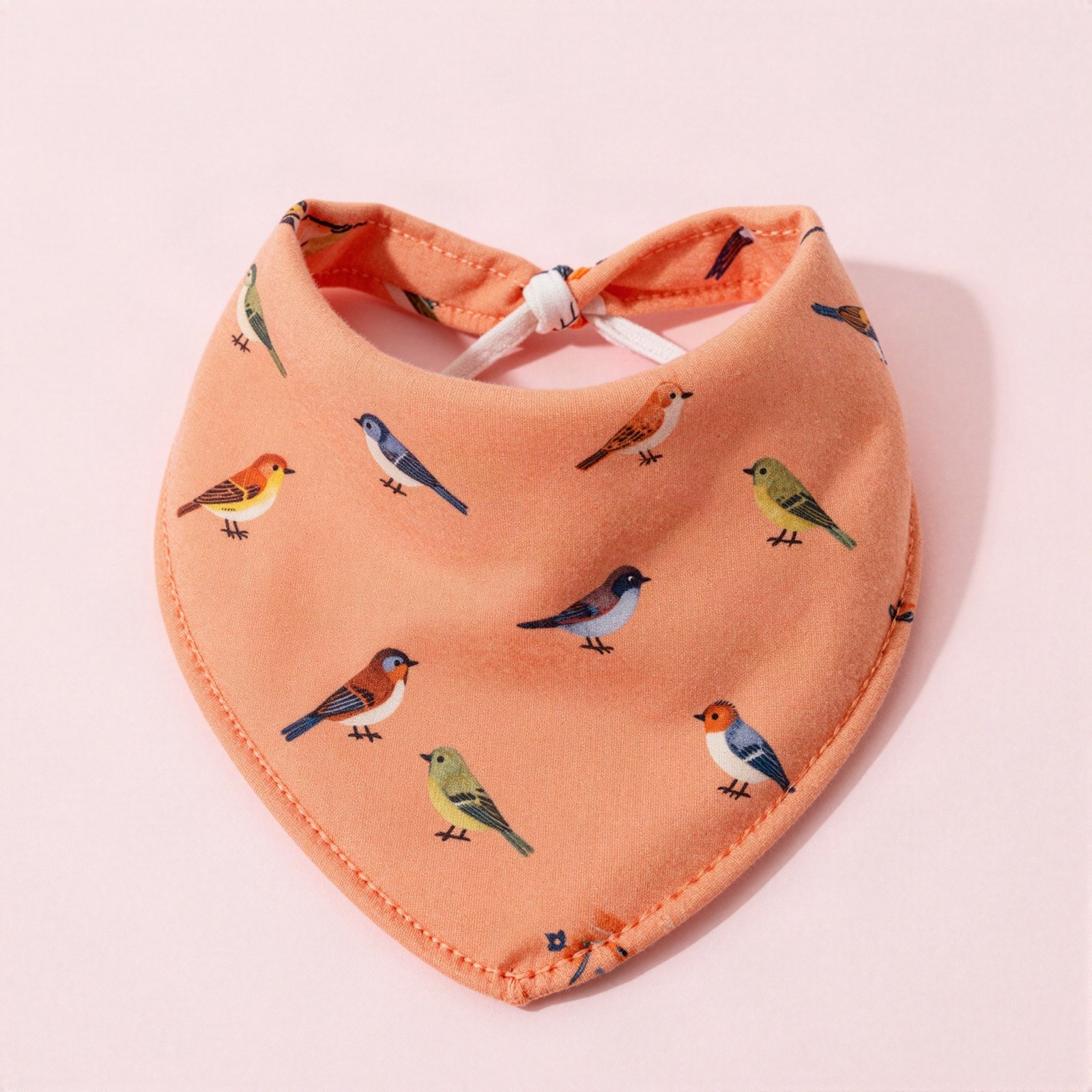 An orange cotton baby bandana bib with an all-over print of small colourful songbirds, laid flat