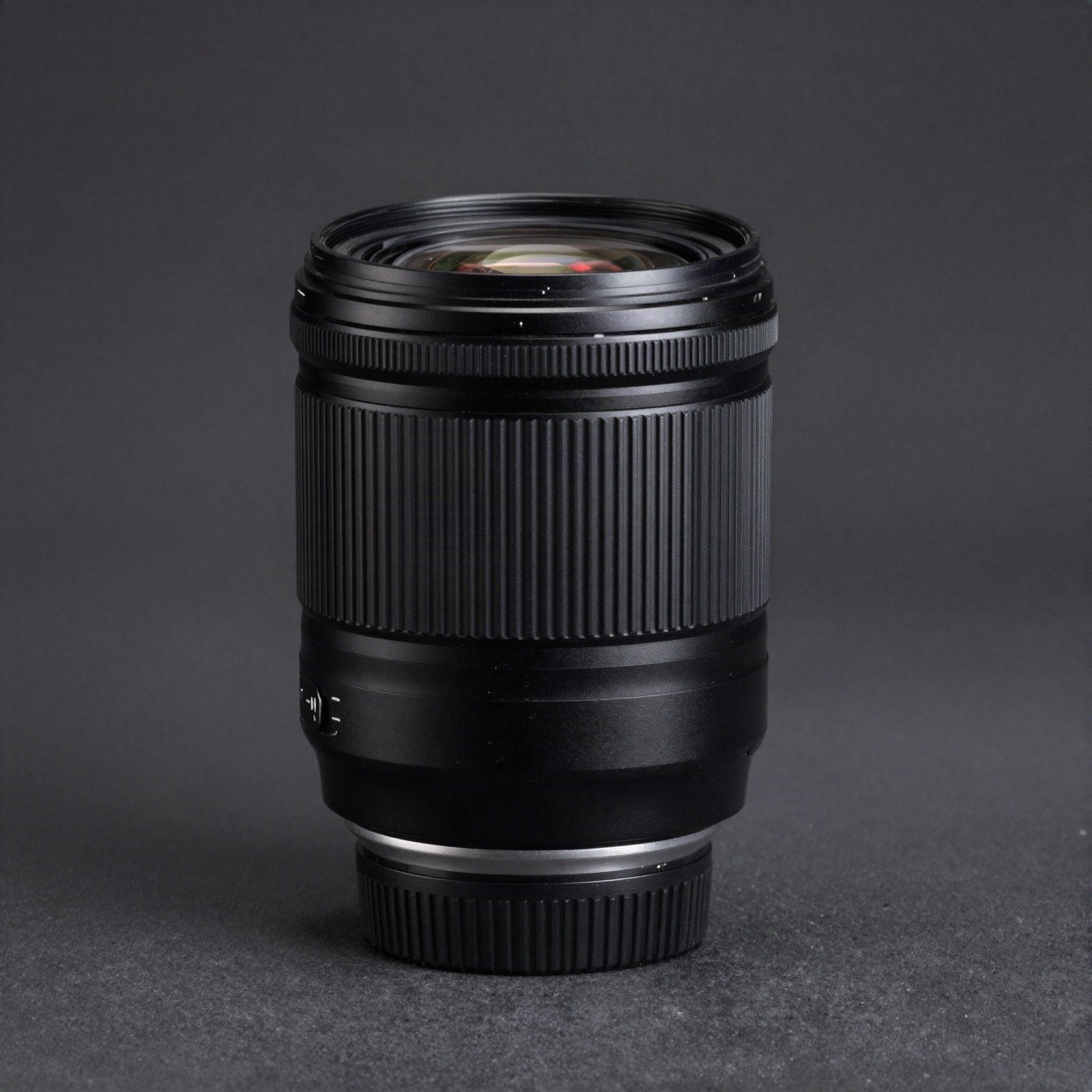 A black camera lens standing upright on a dark background with a red rim light