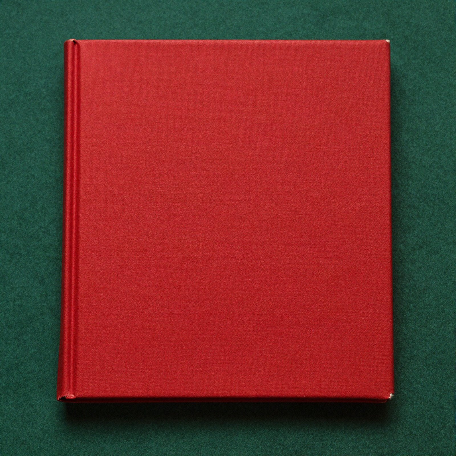 A plain crimson hardcover book on a green felt card table