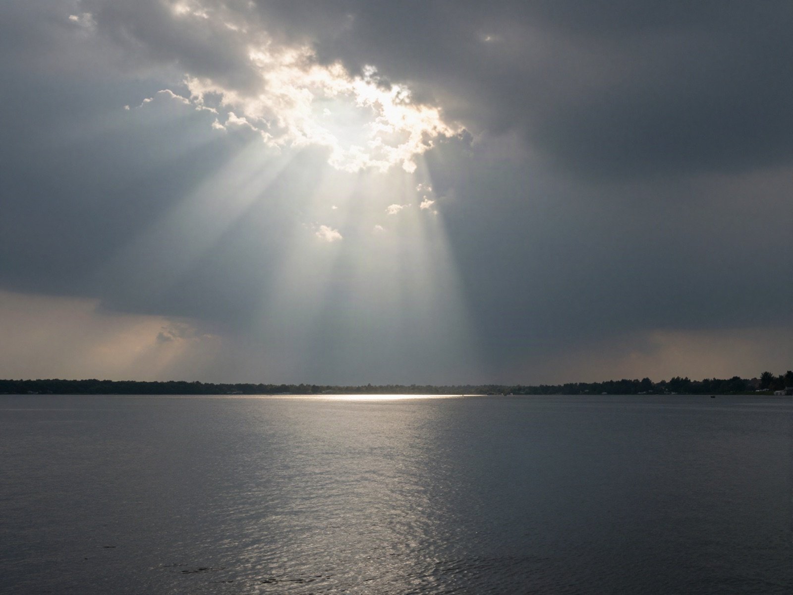 Sunbeams breaking through storm clouds over a calm lake