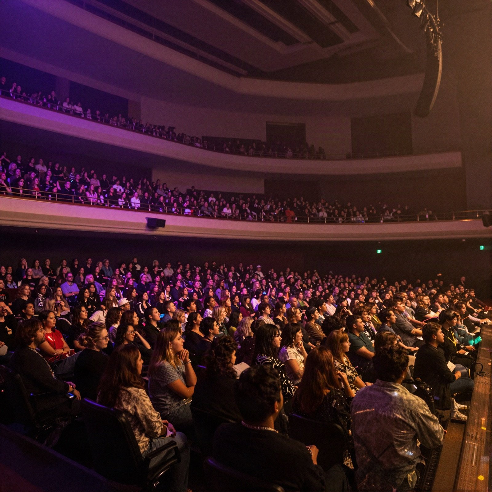 A full concert hall with purple lights over the audience