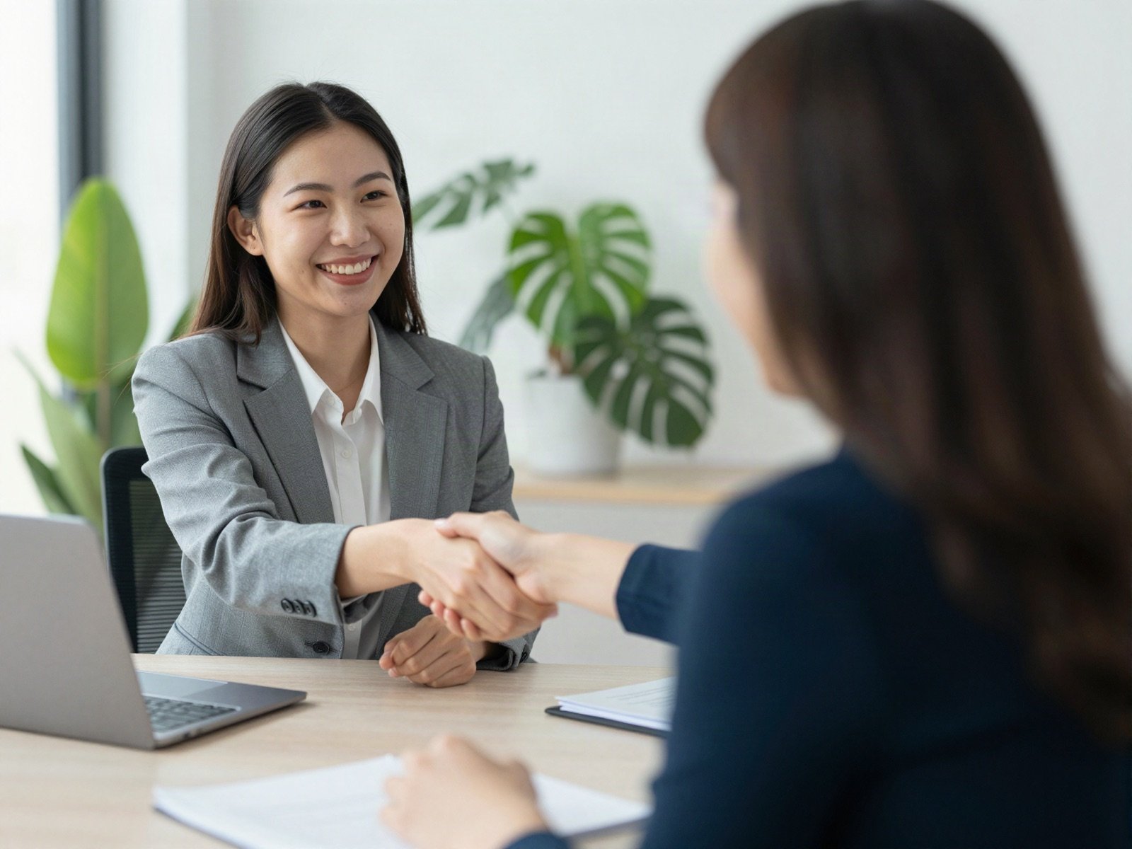 A smiling financial advisor shaking hands with a client across a desk