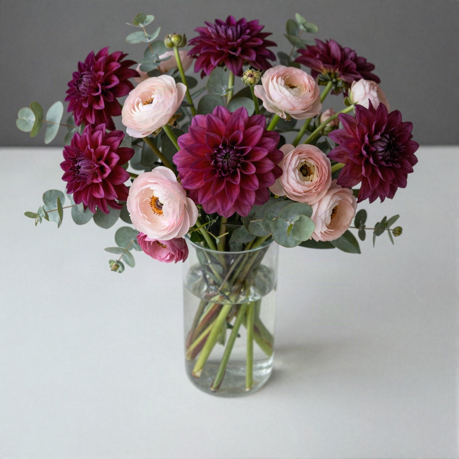 Seasonal bouquet of magenta dahlias, blush ranunculus and eucalyptus in a glass vase