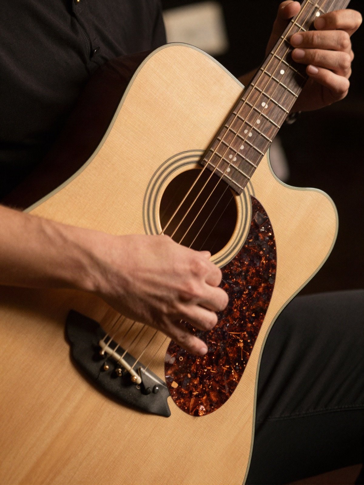 Hands tapping percussive rhythms on the body of an acoustic guitar