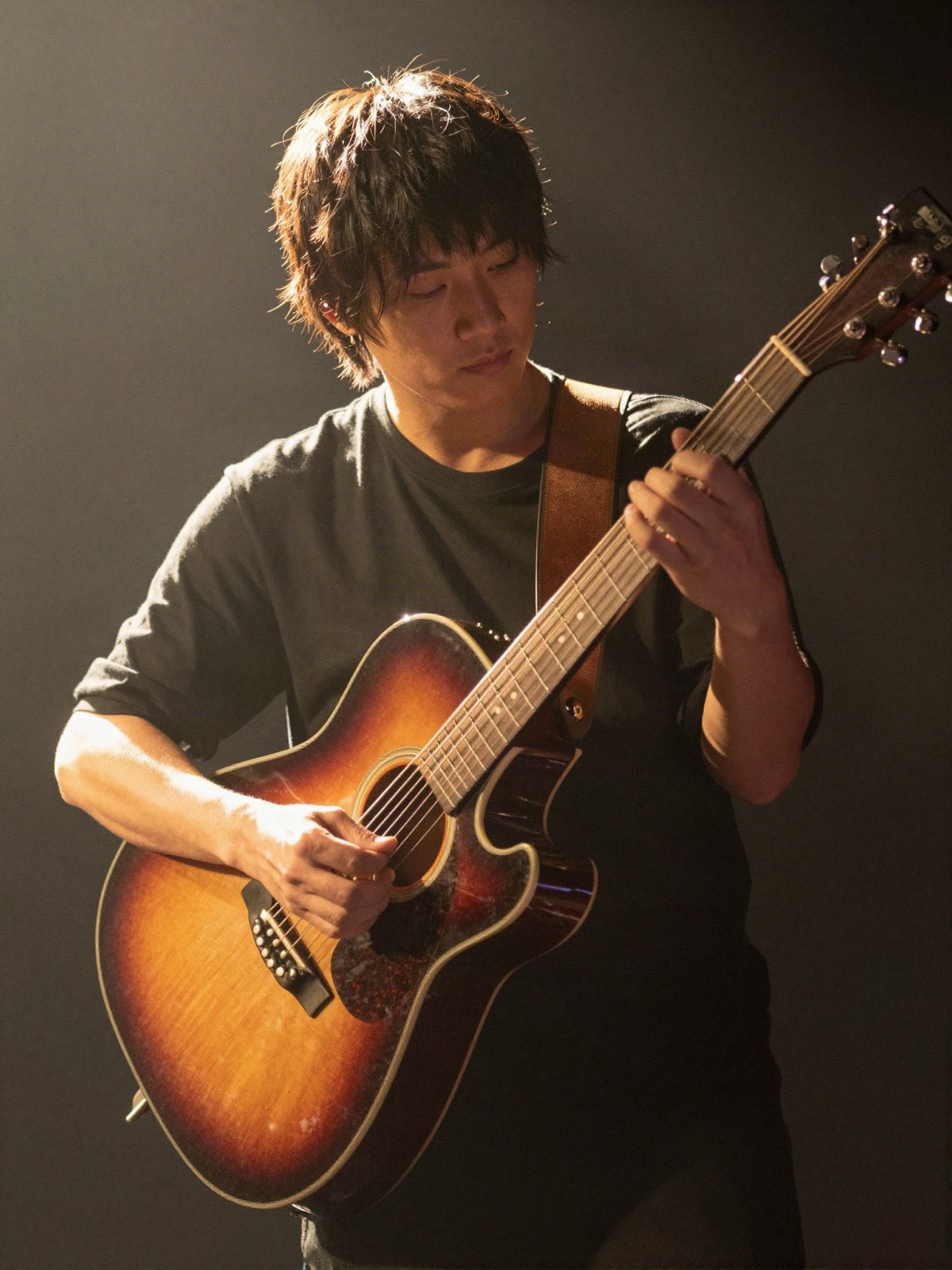 A guitarist strumming a sunburst acoustic guitar in warm backlight