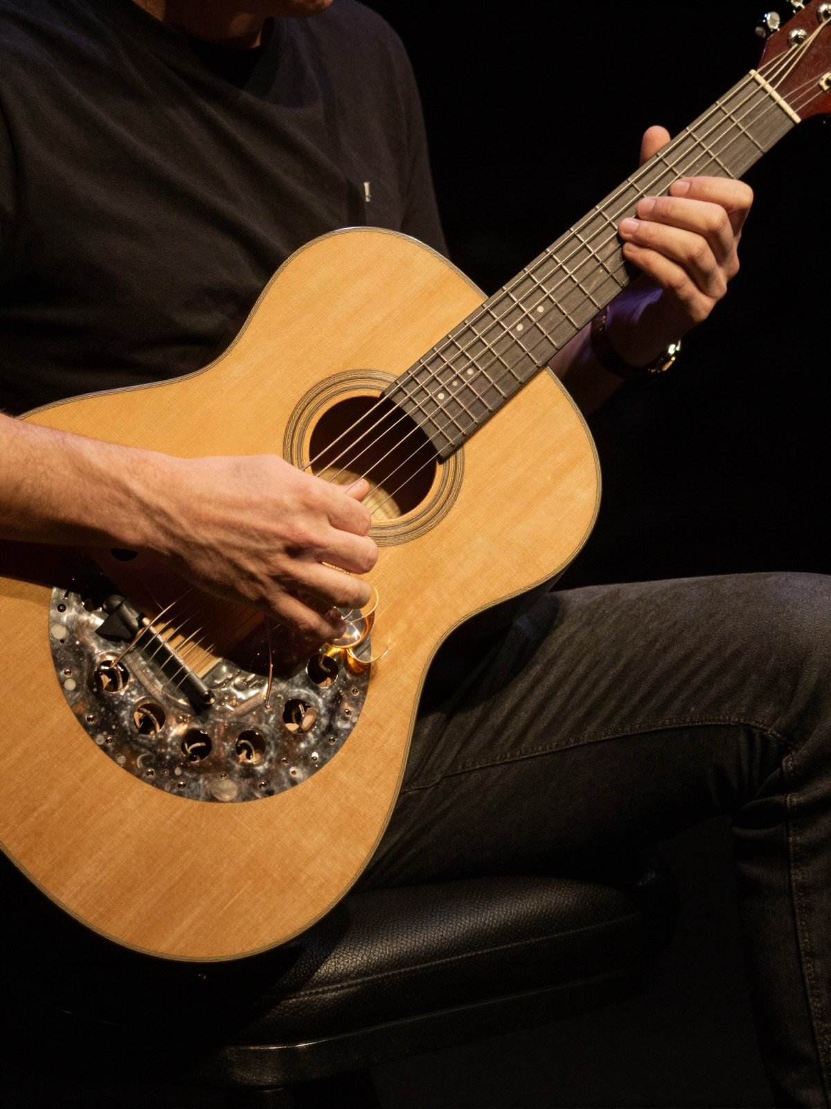 Close-up of a guitarist playing an acoustic guitar seated in a dark room