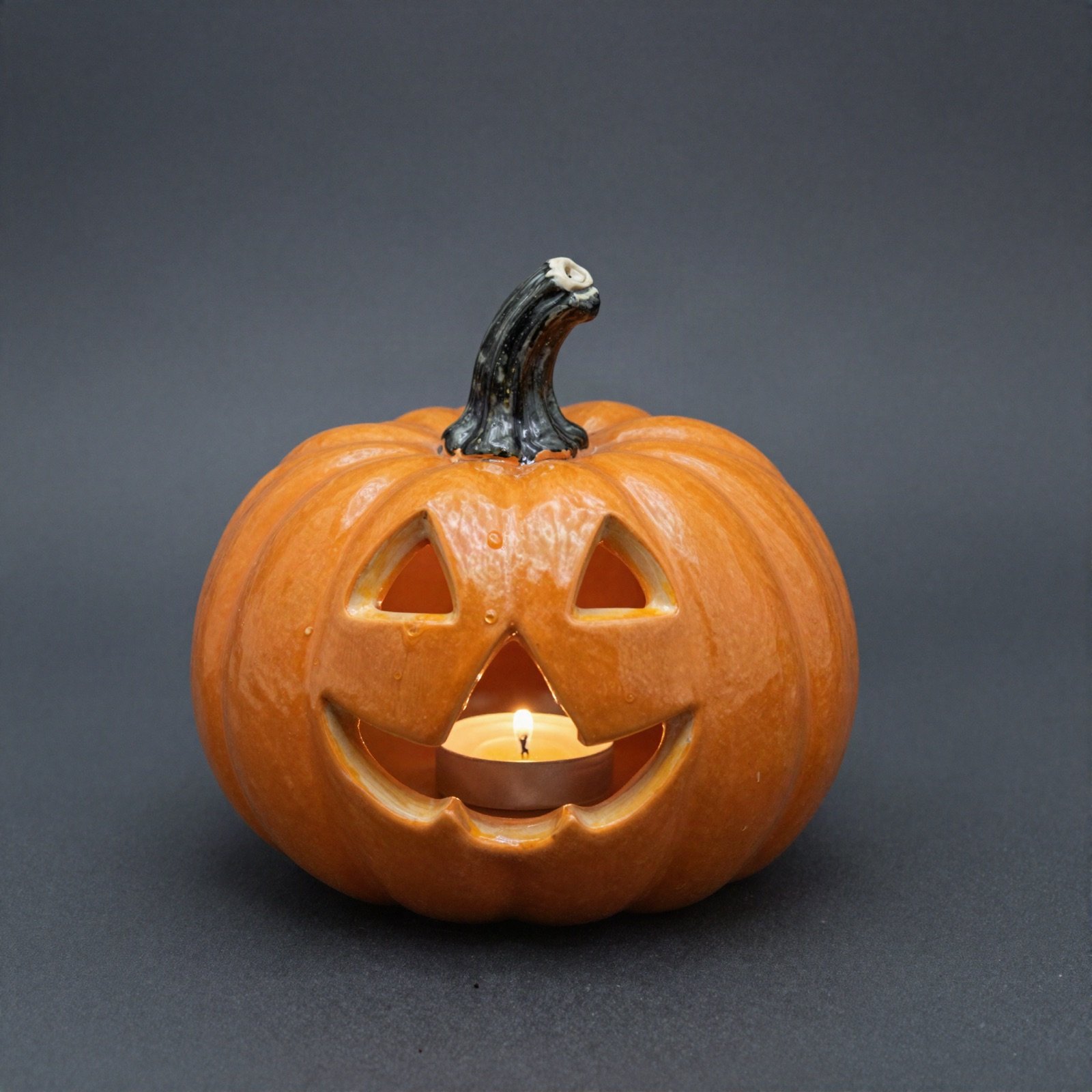 An orange ceramic jack-o-lantern pumpkin glowing with a tea light