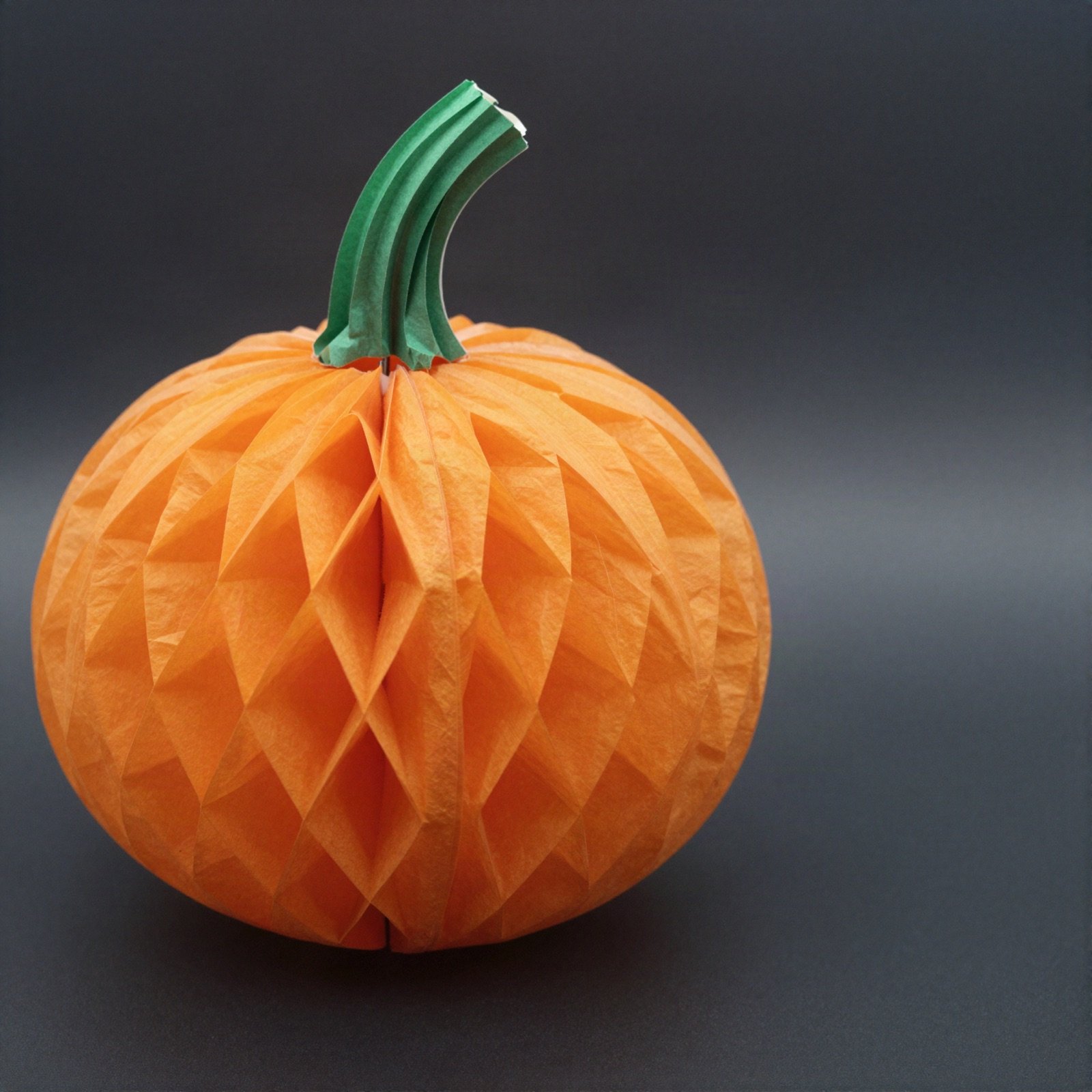 An orange paper honeycomb pumpkin with a green stem