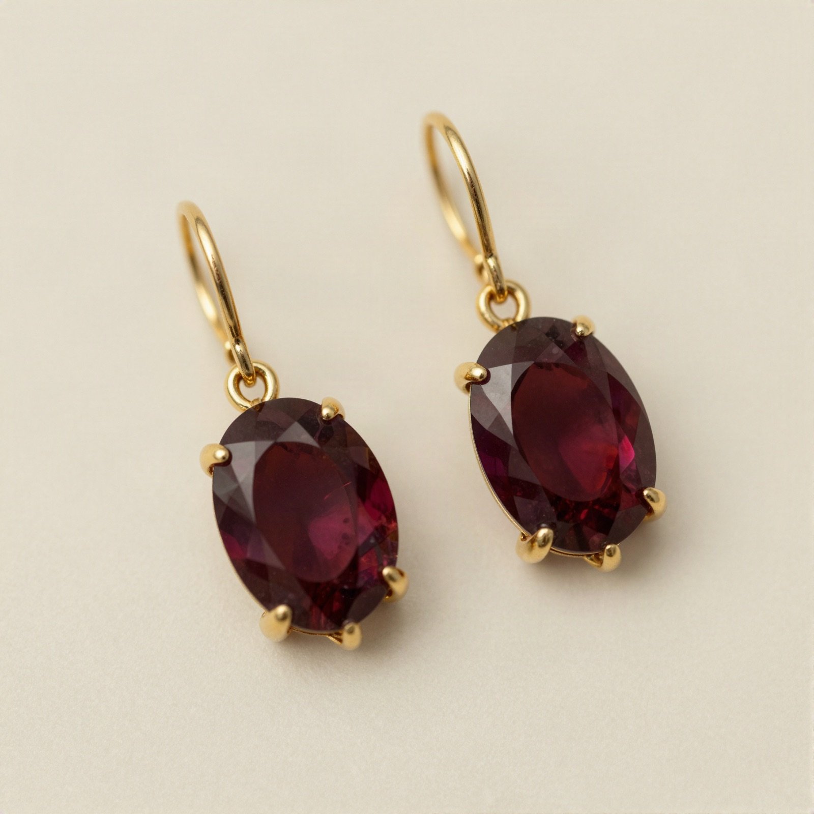 Pair of oval maroon stone drop earrings in gold claw settings