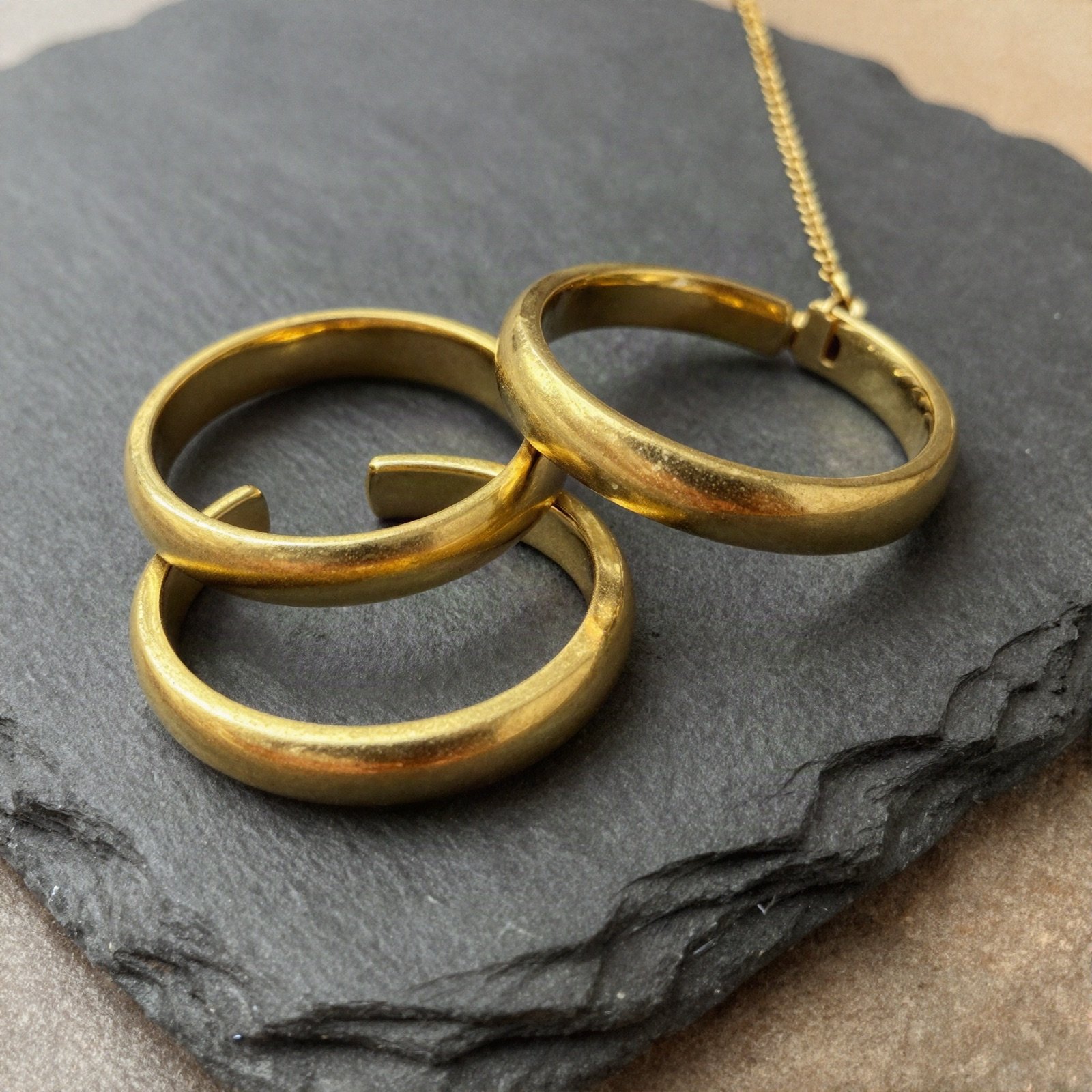 Three polished gold rings and a gold chain on dark slate