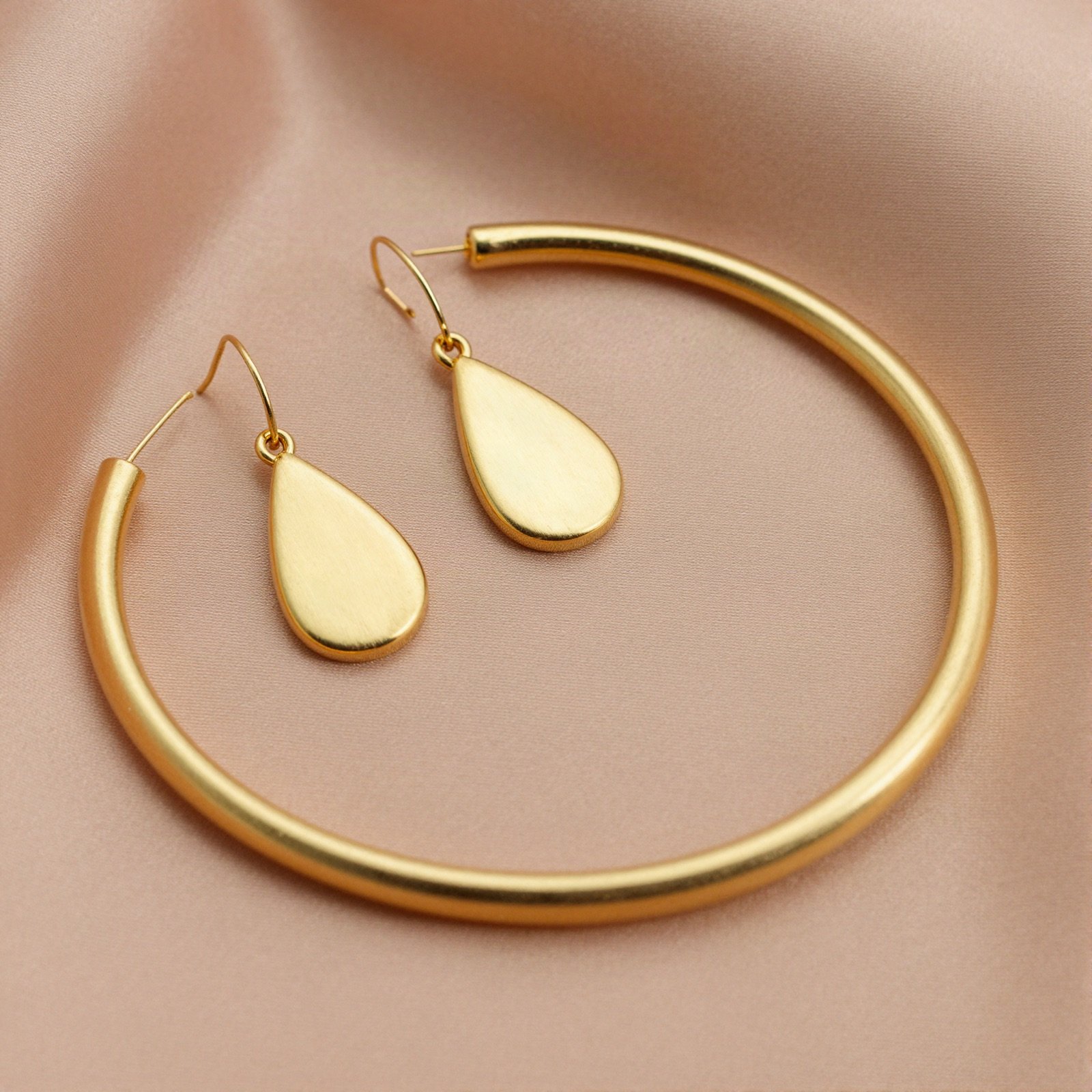 Gold teardrop earrings and a gold bangle on peach silk