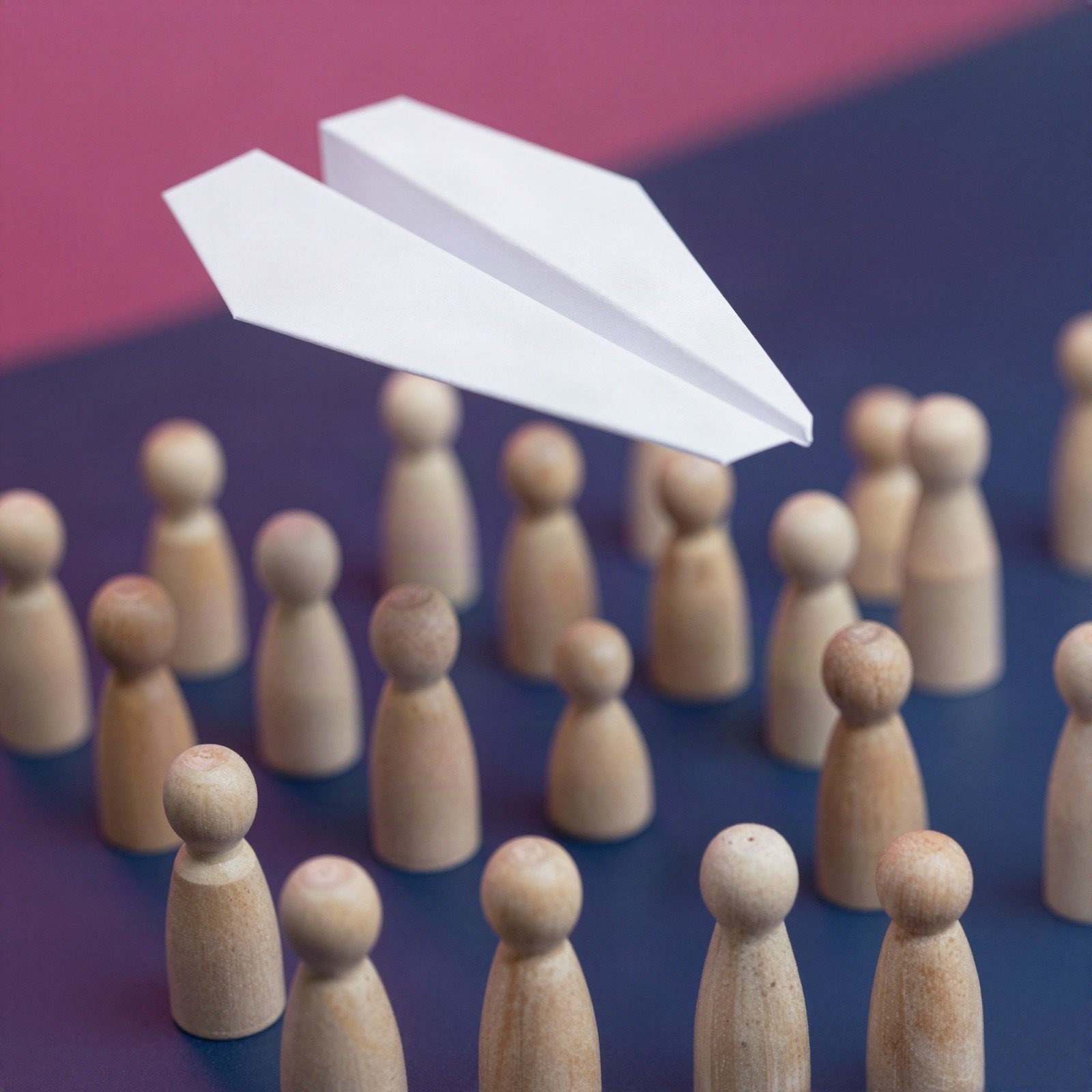 Paper airplane gliding above a crowd of small wooden figures