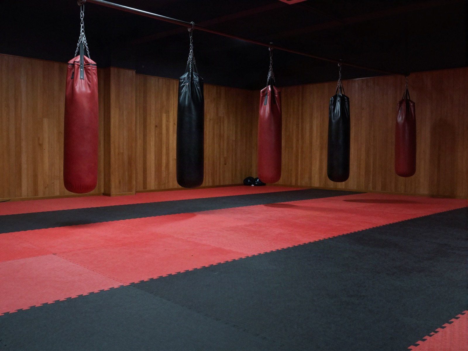 Empty dojo with red and black mats and hanging heavy bags