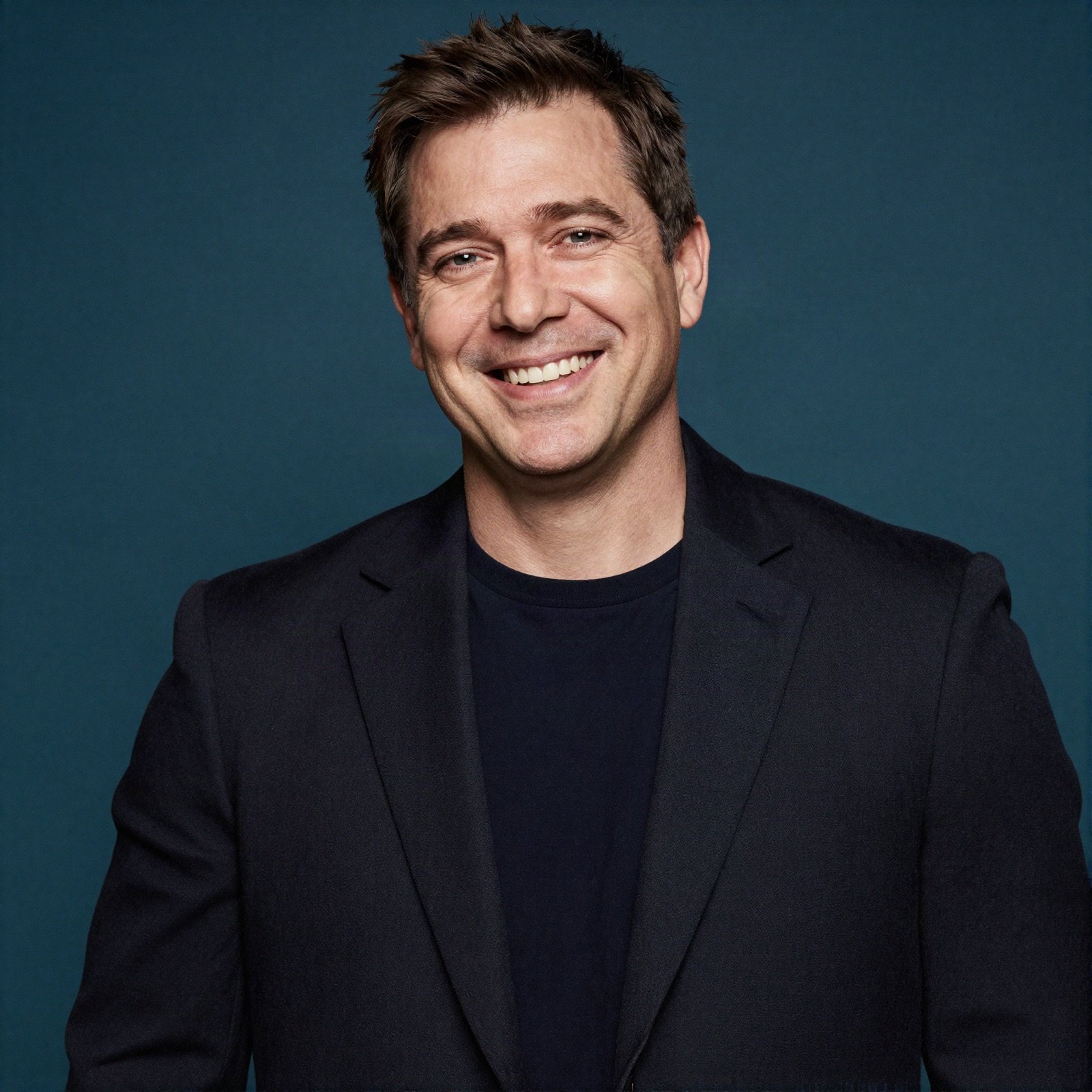 Smiling man in a black blazer against a dark teal background