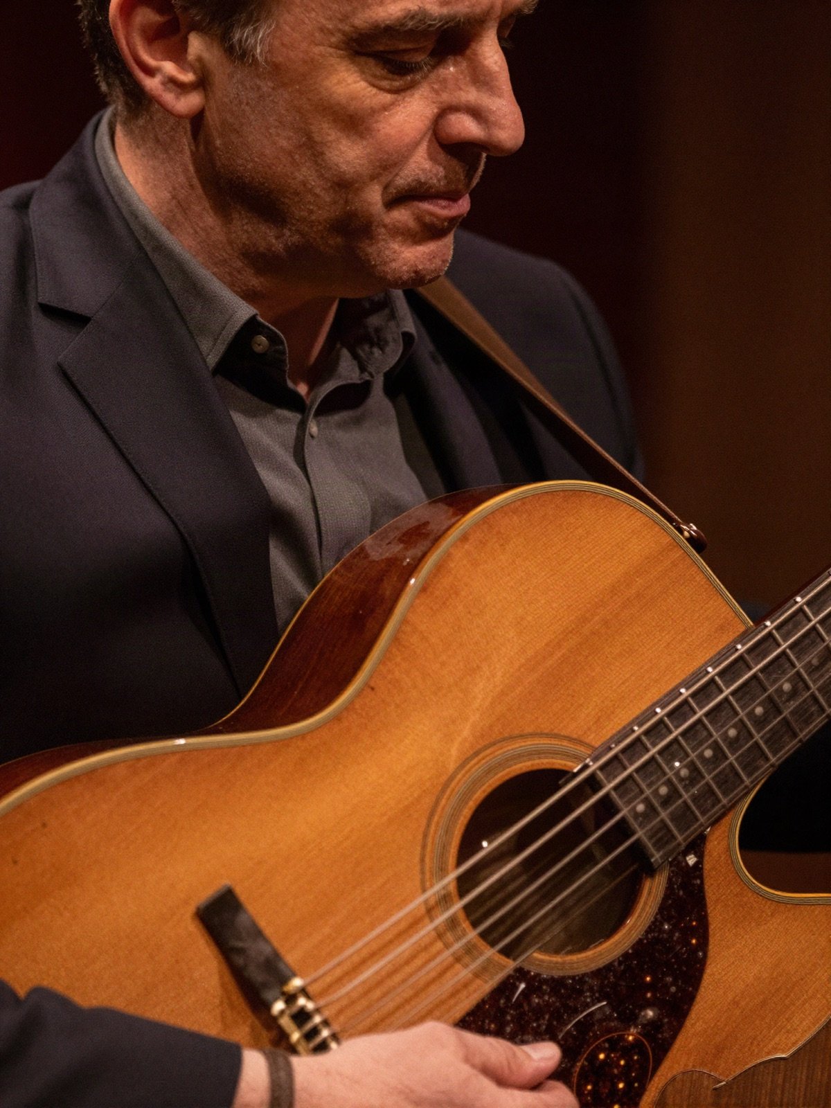 A jazz guitarist in a dark suit playing an acoustic guitar in a dim club