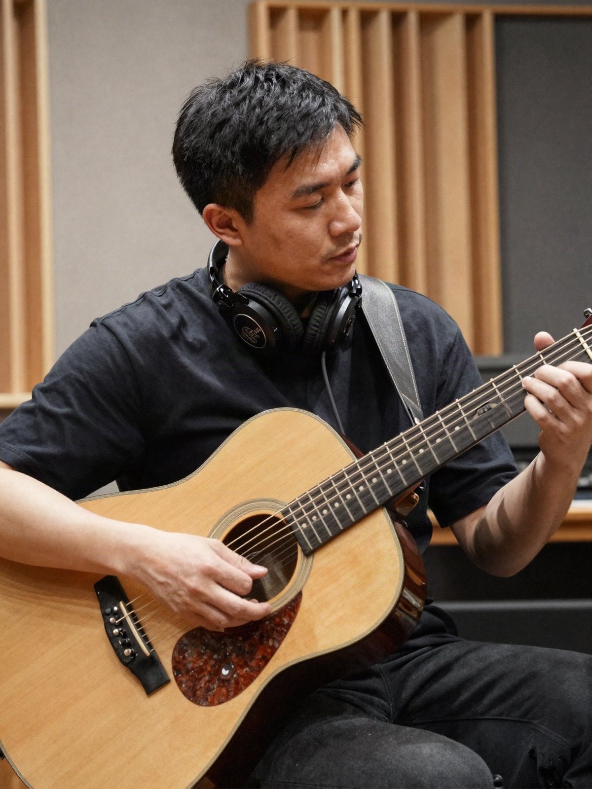 A session guitarist with headphones playing an acoustic guitar in a studio