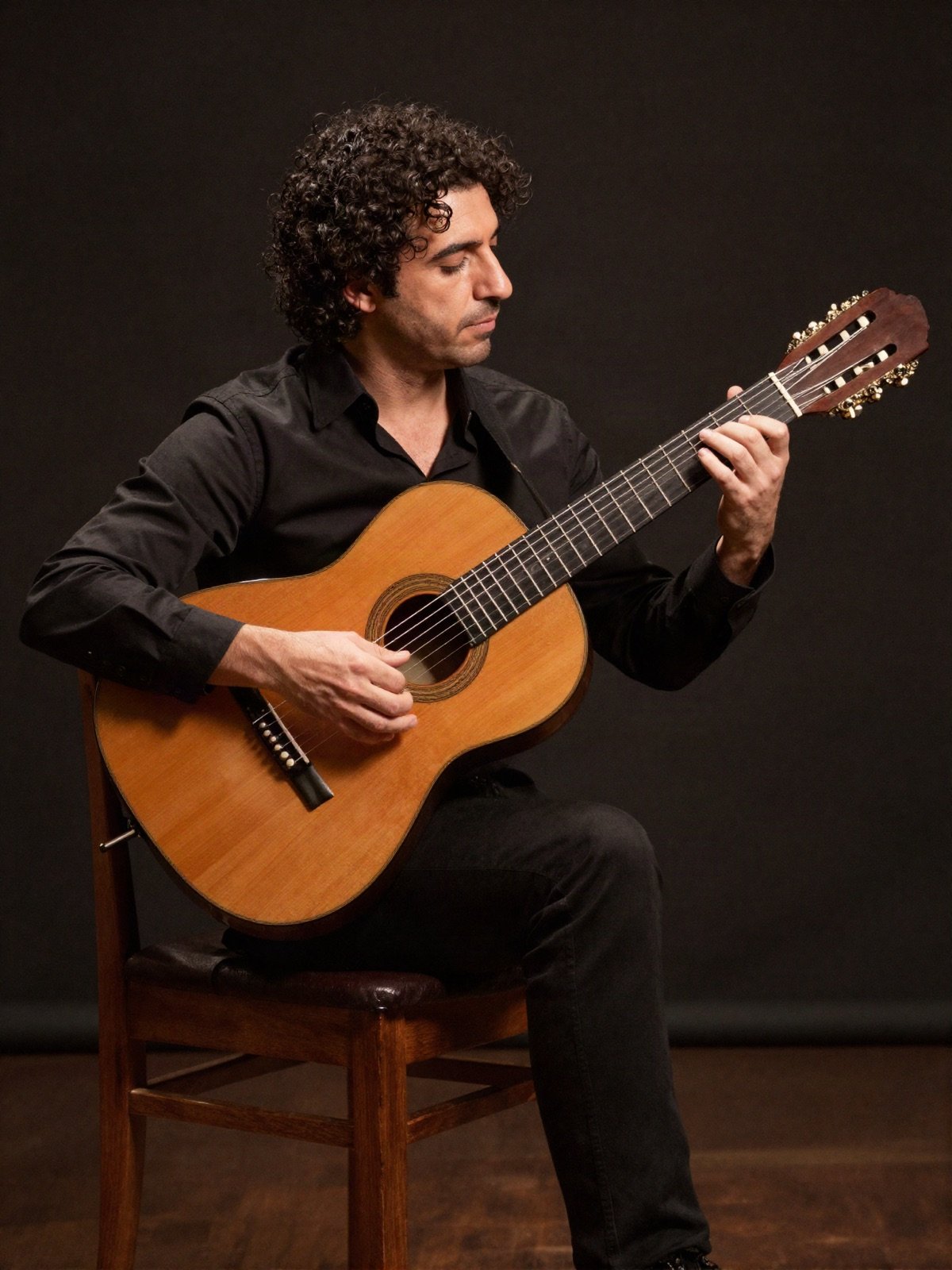 A classical guitarist playing a nylon-string guitar on a wooden chair