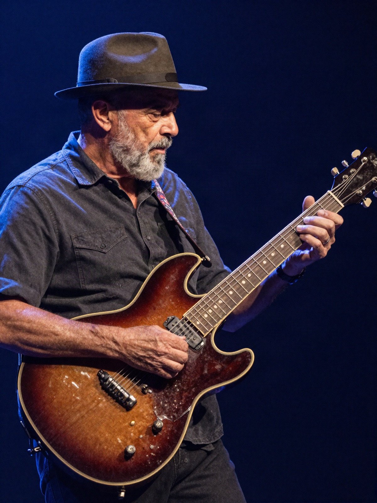 A blues guitarist in a hat playing a sunburst electric guitar on stage