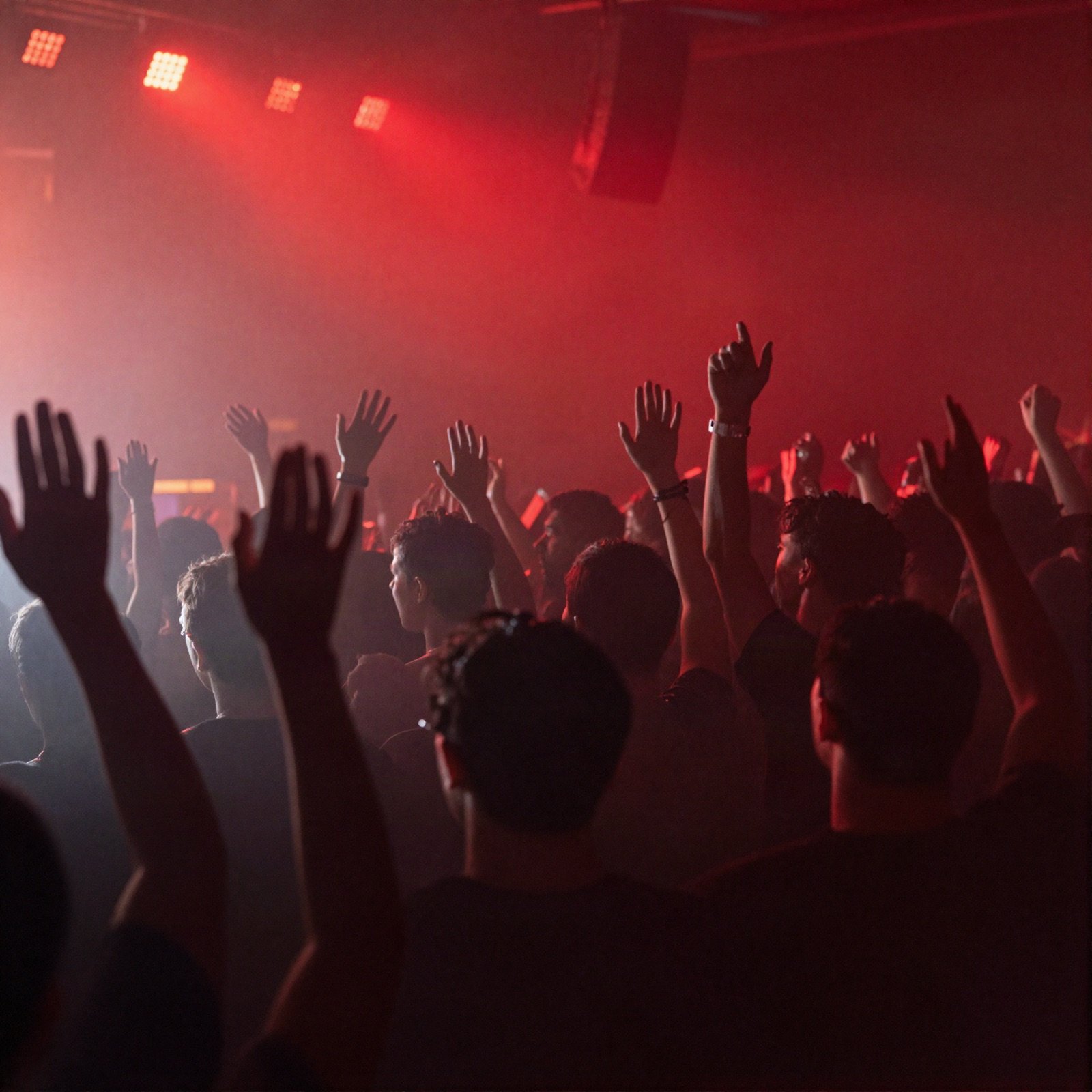 A concert crowd raising their hands toward red stage lights