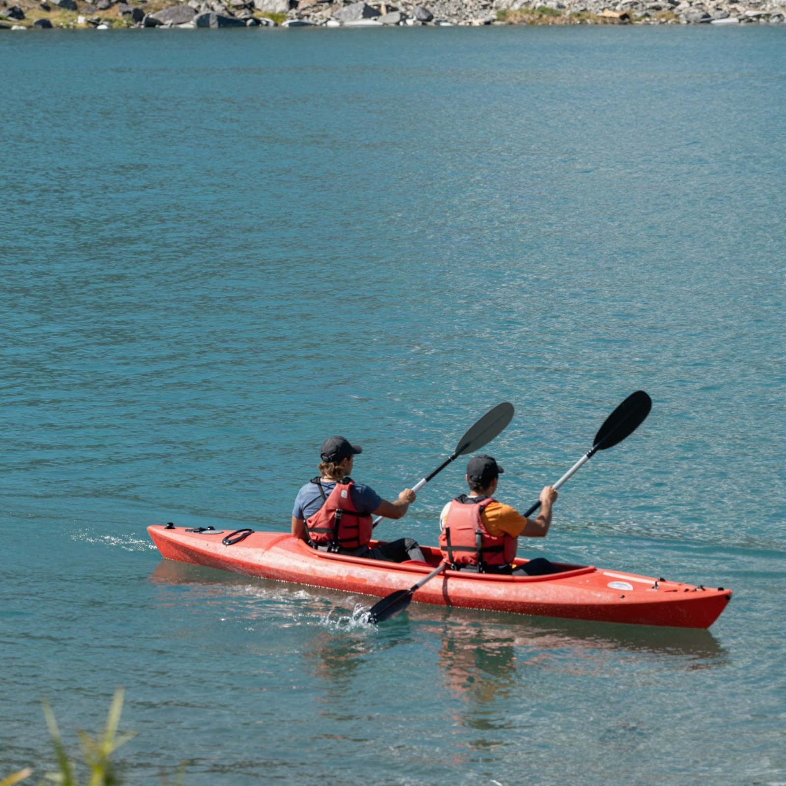 Two people paddling a red tandem kayak on a turquoise lake