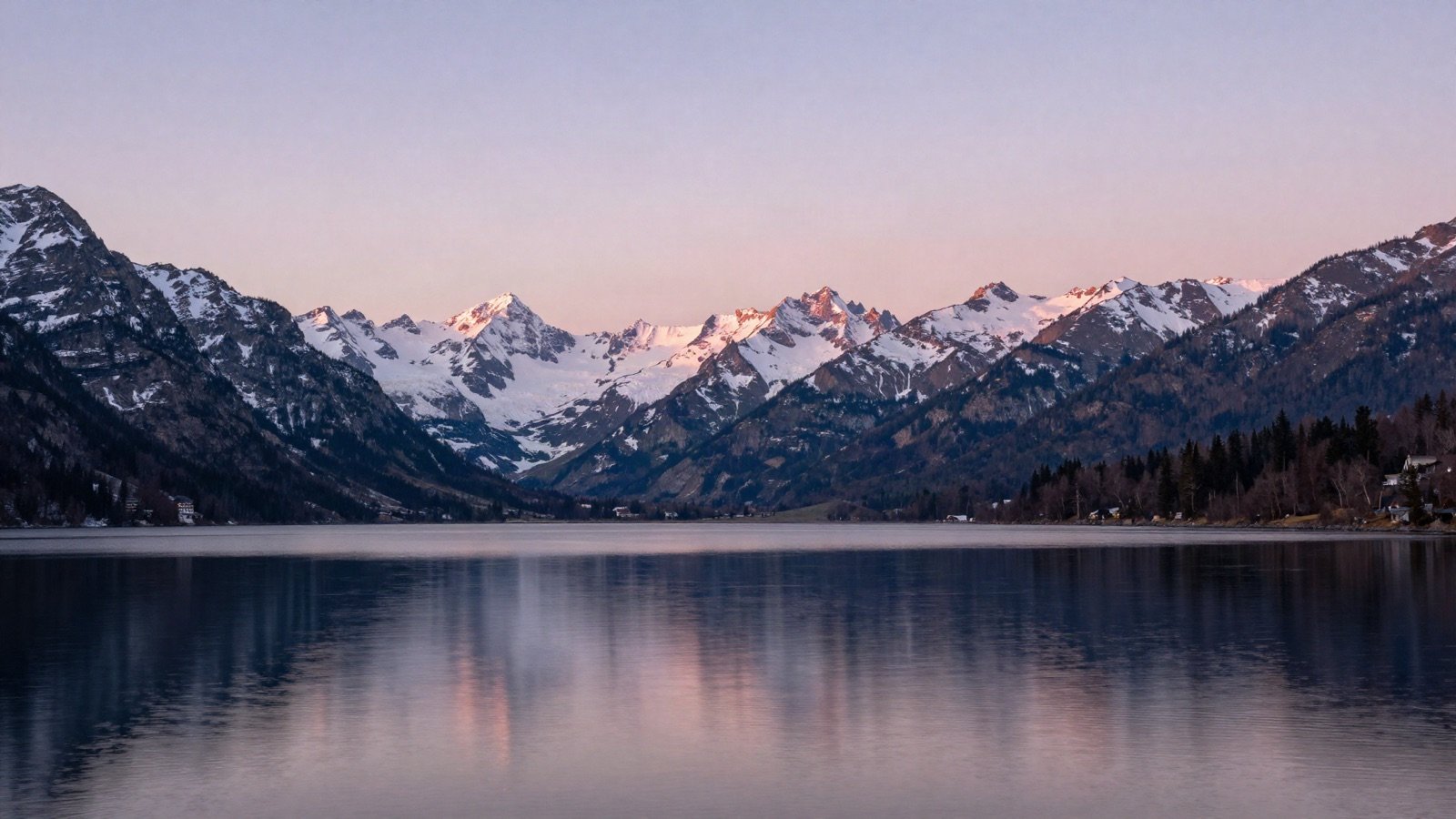 A calm mountain lake reflecting snowy peaks at sunrise