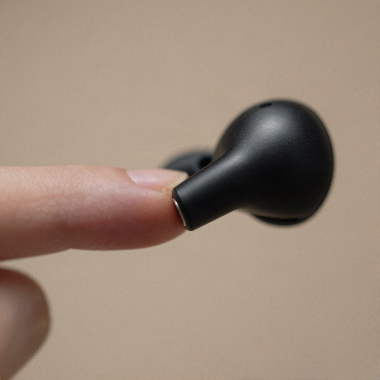 Fingertip touching the control surface of a black wireless earbud