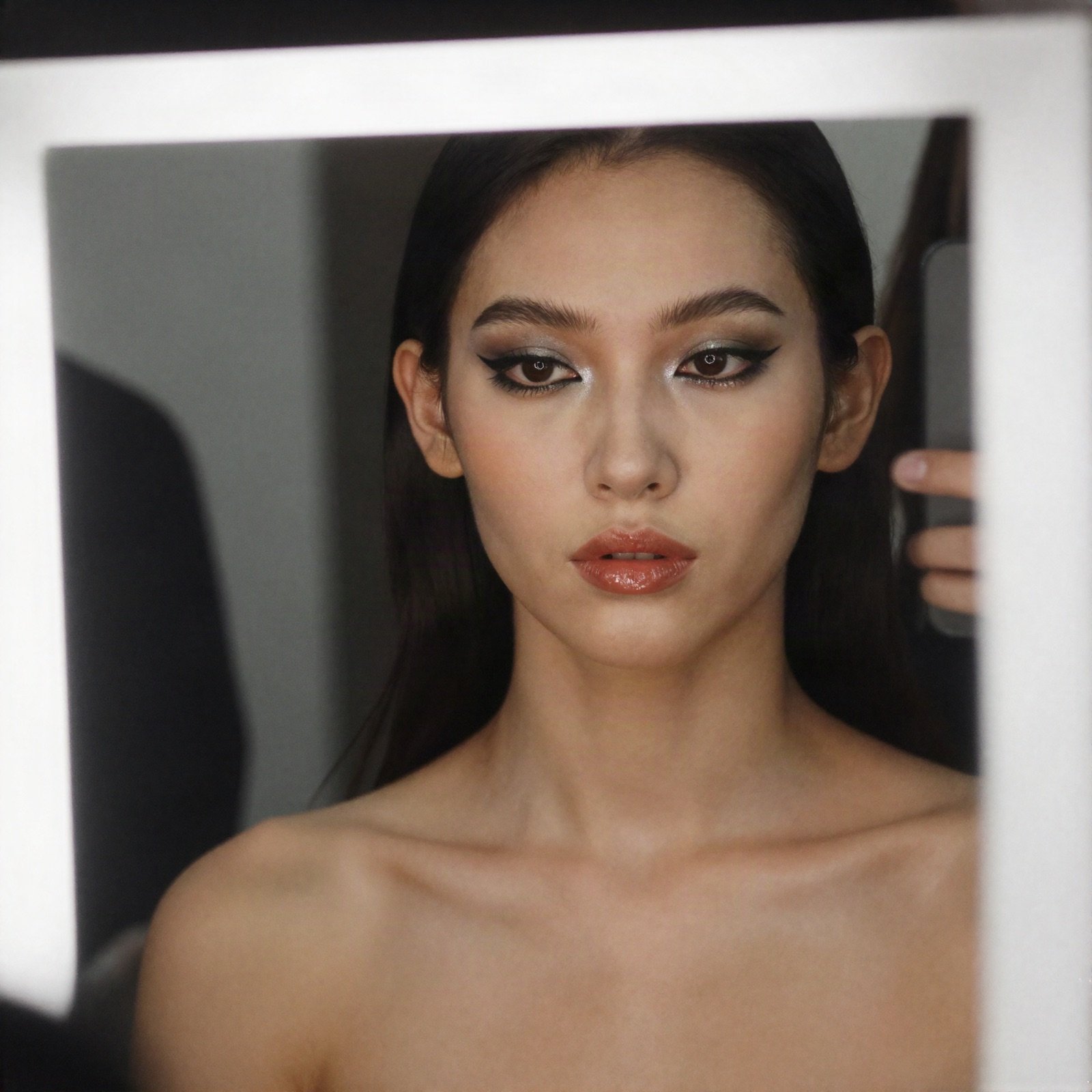 Model with graphic eyeliner and glossy lips reflected in a lit mirror