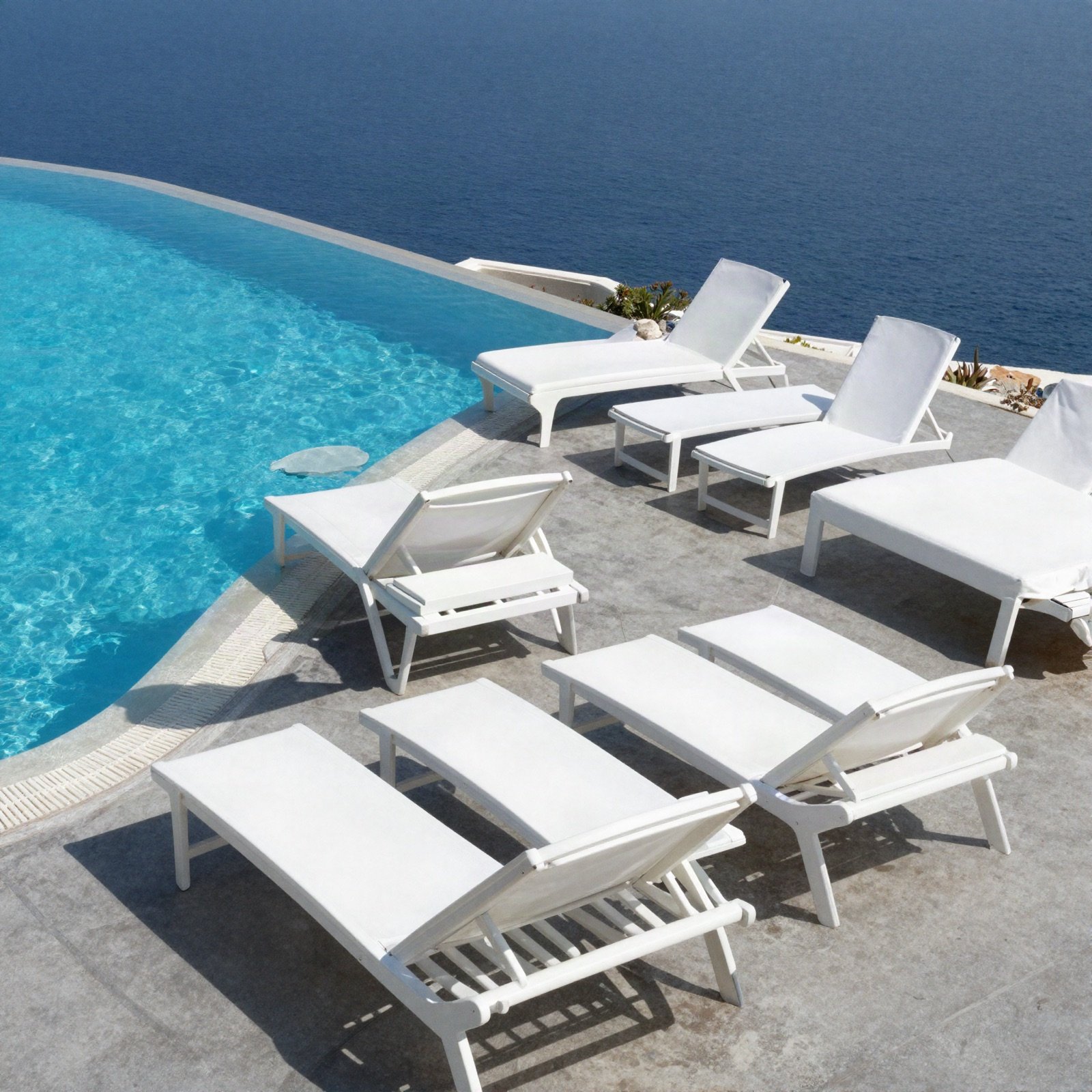 Infinity-edge pool with white sun loungers overlooking the sea