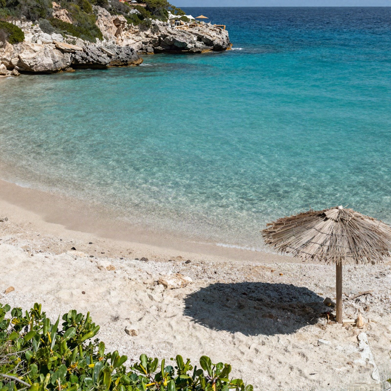 Sandy cove with clear turquoise water and a straw parasol