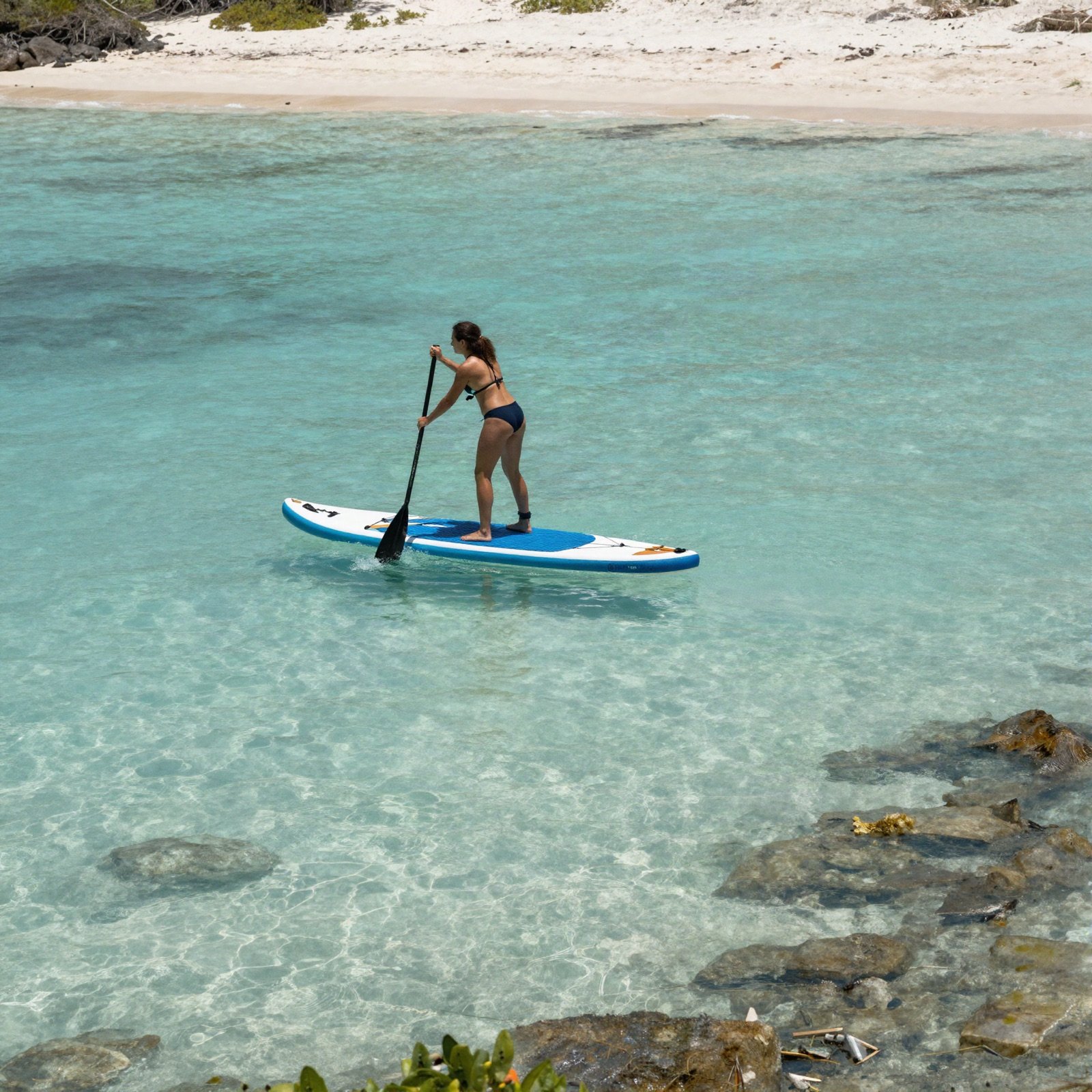 Woman paddleboarding across a clear lagoon near a sandy beach