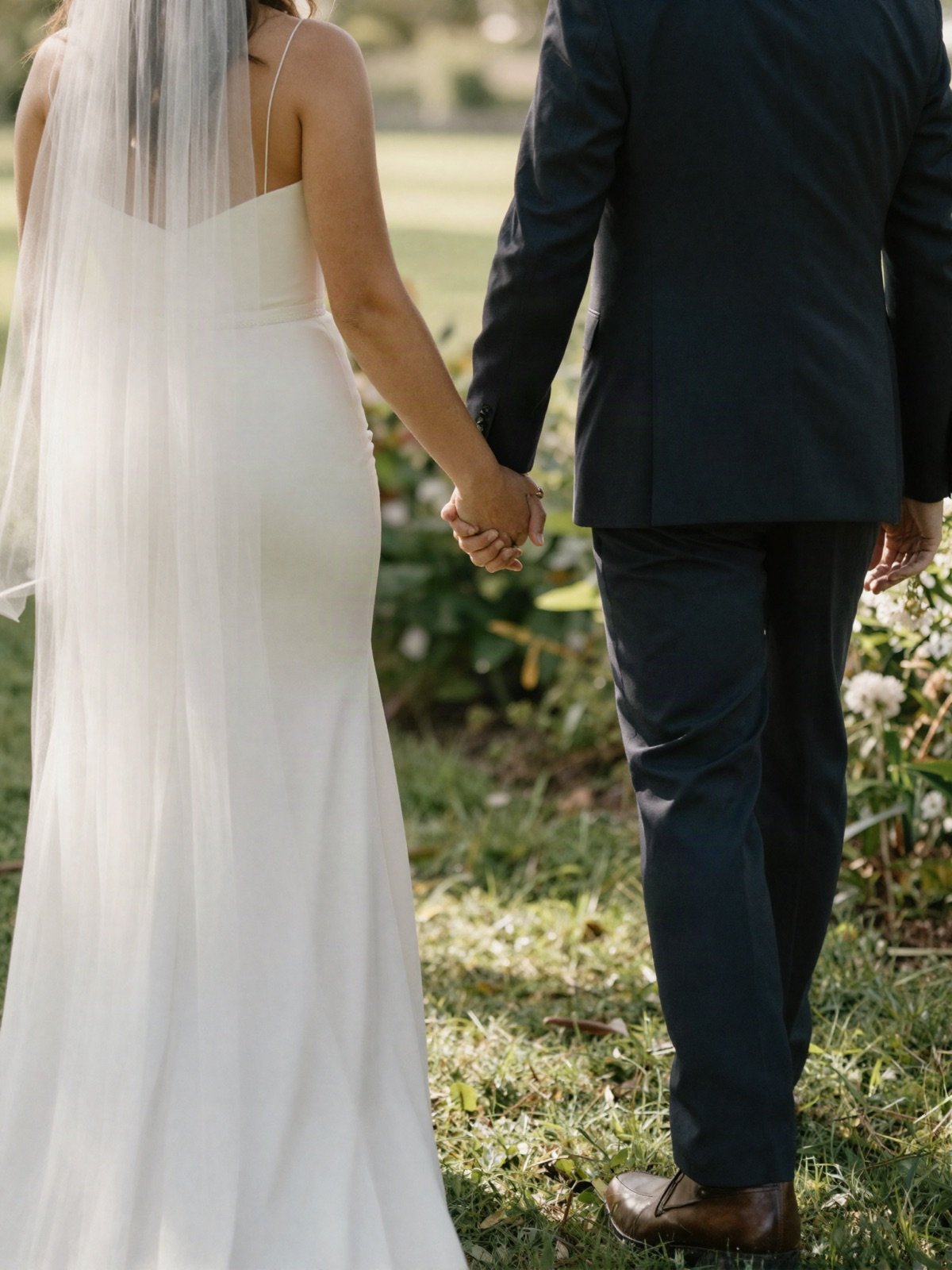 The bride and groom walking hand in hand through a garden