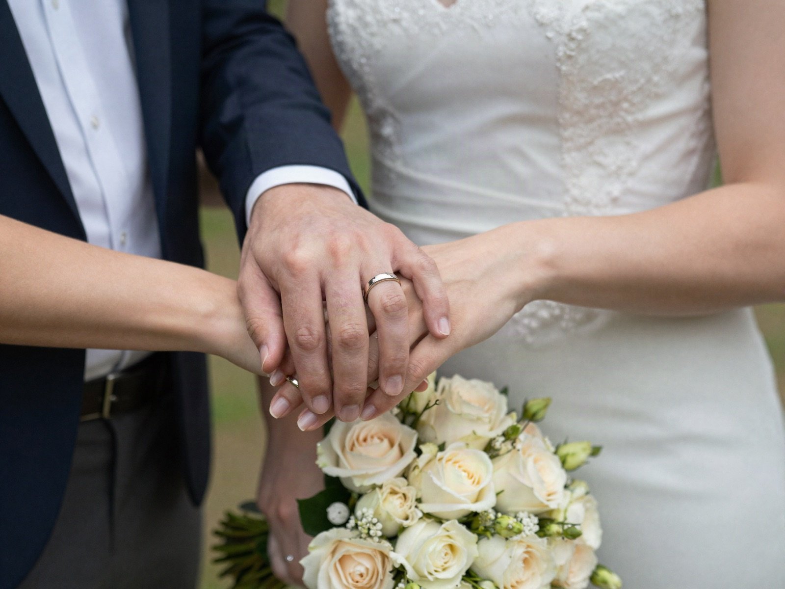 The couple holding hands with their wedding rings and a bouquet of roses