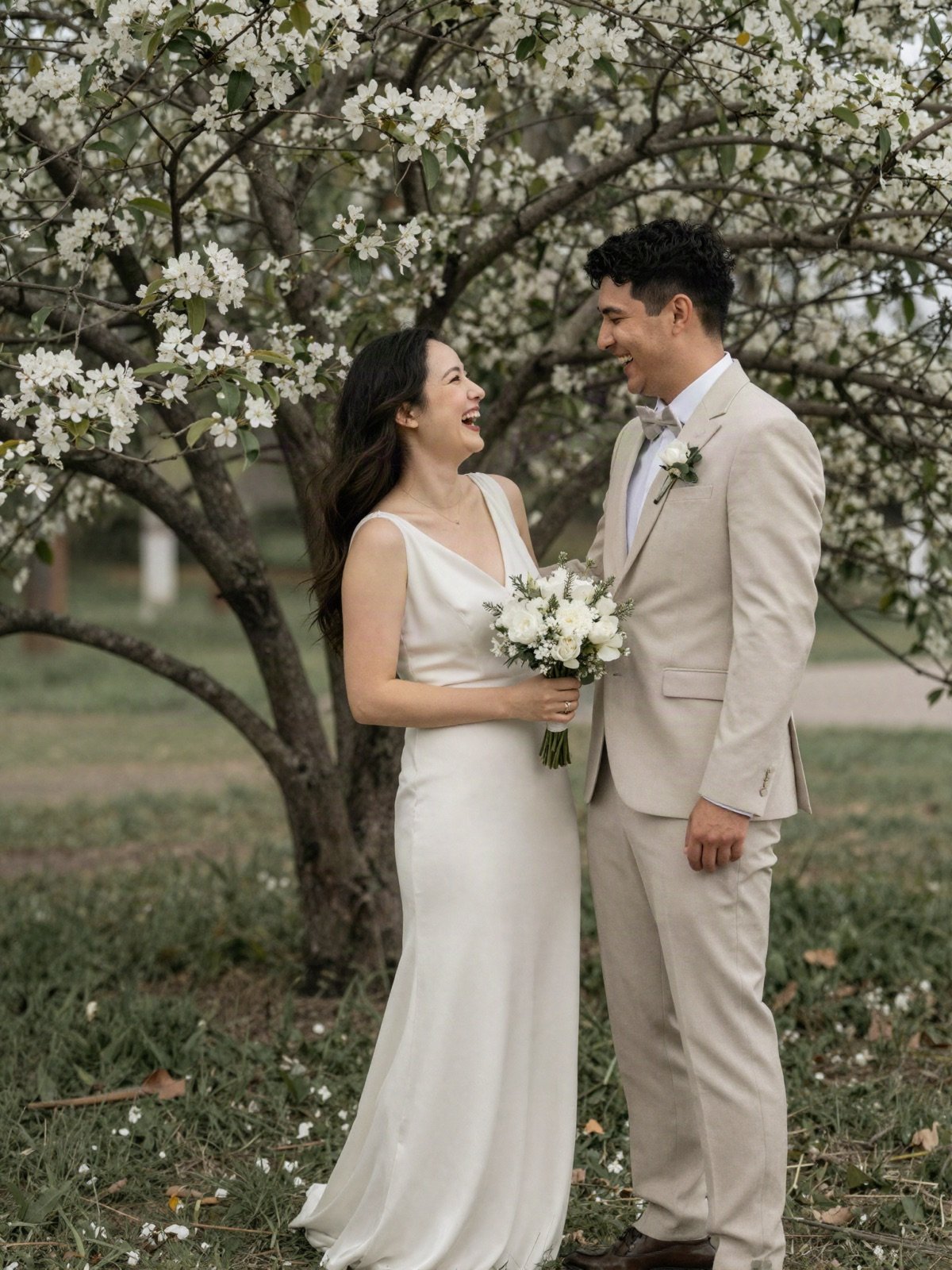 Bride and groom laughing together under a blossoming tree