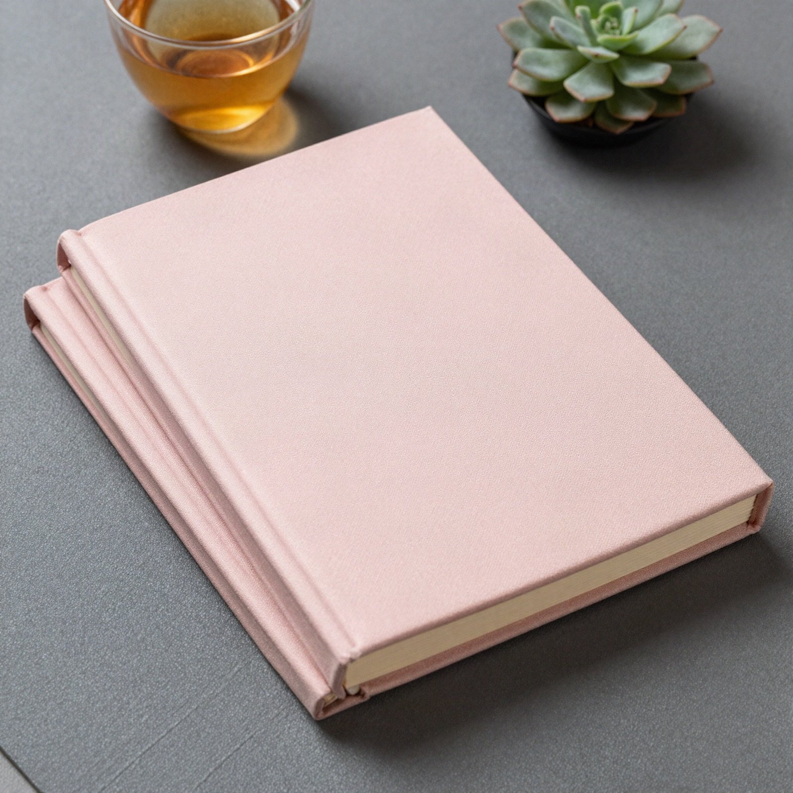 Pink hardcover book on a mat beside herbal tea and a succulent